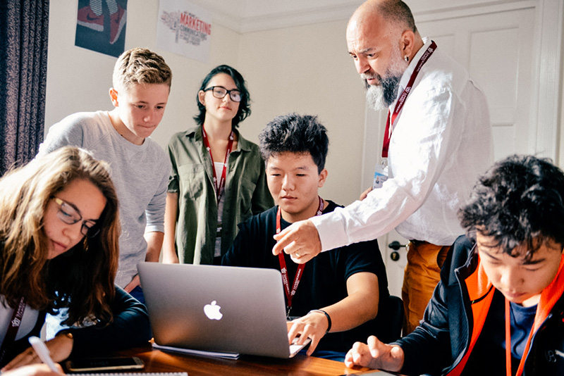 students and teacher in classroom looking at a laptop lowres