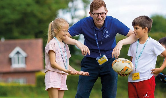 Activity-leader-with-two-summer-school-students-playing-on-field