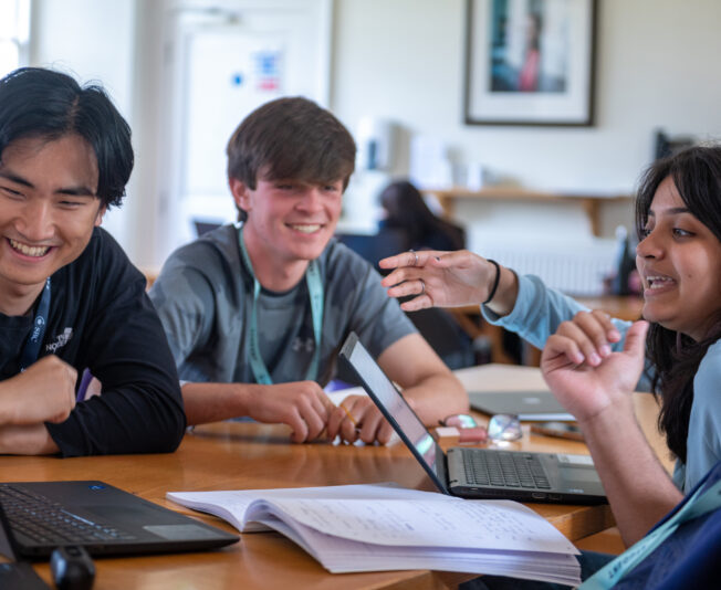 Engaging diverse group of young students at summer boarding courses, collaborating with laptops and notebooks.