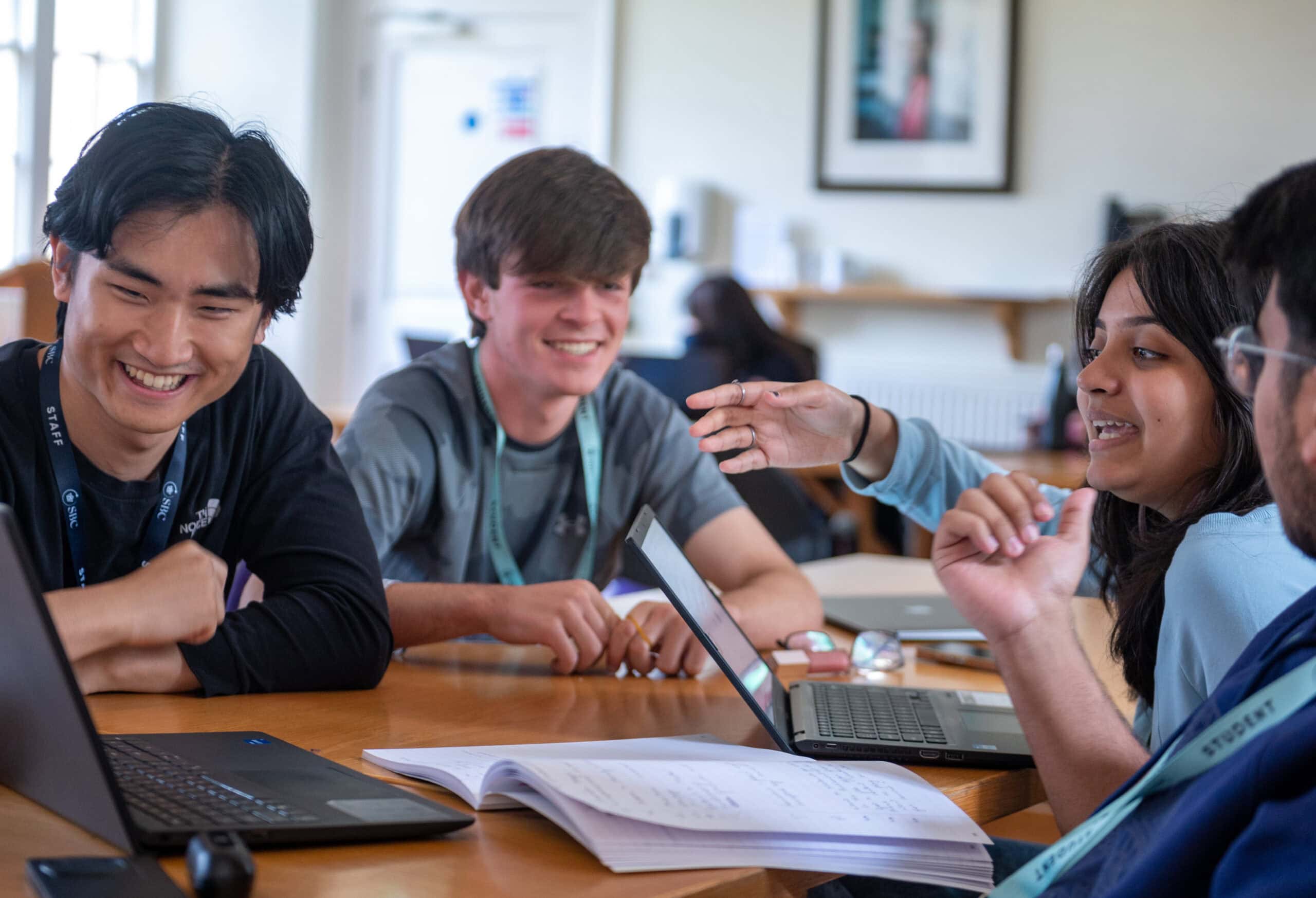 Engaging diverse group of young students at summer boarding courses, collaborating with laptops and notebooks.