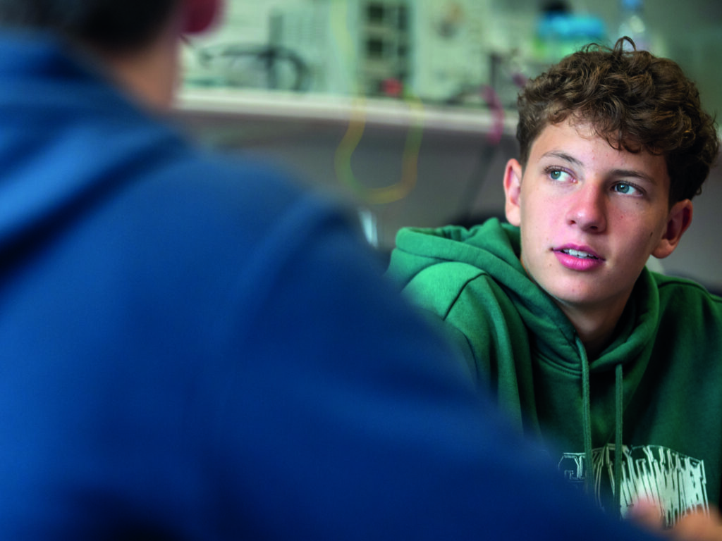 Enthusiastic teenage boy in green hoodie participating in summer boarding course activities at an educational camp.