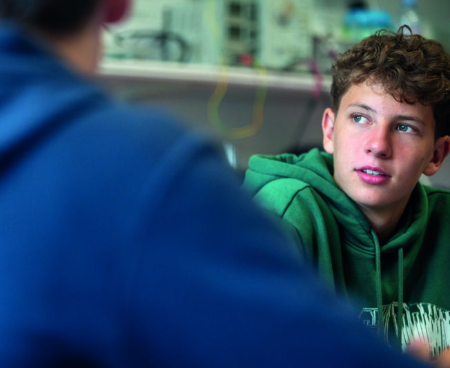 Enthusiastic teenage boy in green hoodie participating in summer boarding course activities at an educational camp.