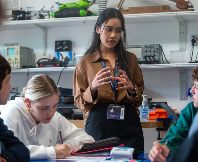 Advanced classroom with diverse students learning and taking notes, led by a young female teacher in a well-equipped lab at Summer Boarding Courses in the UK.