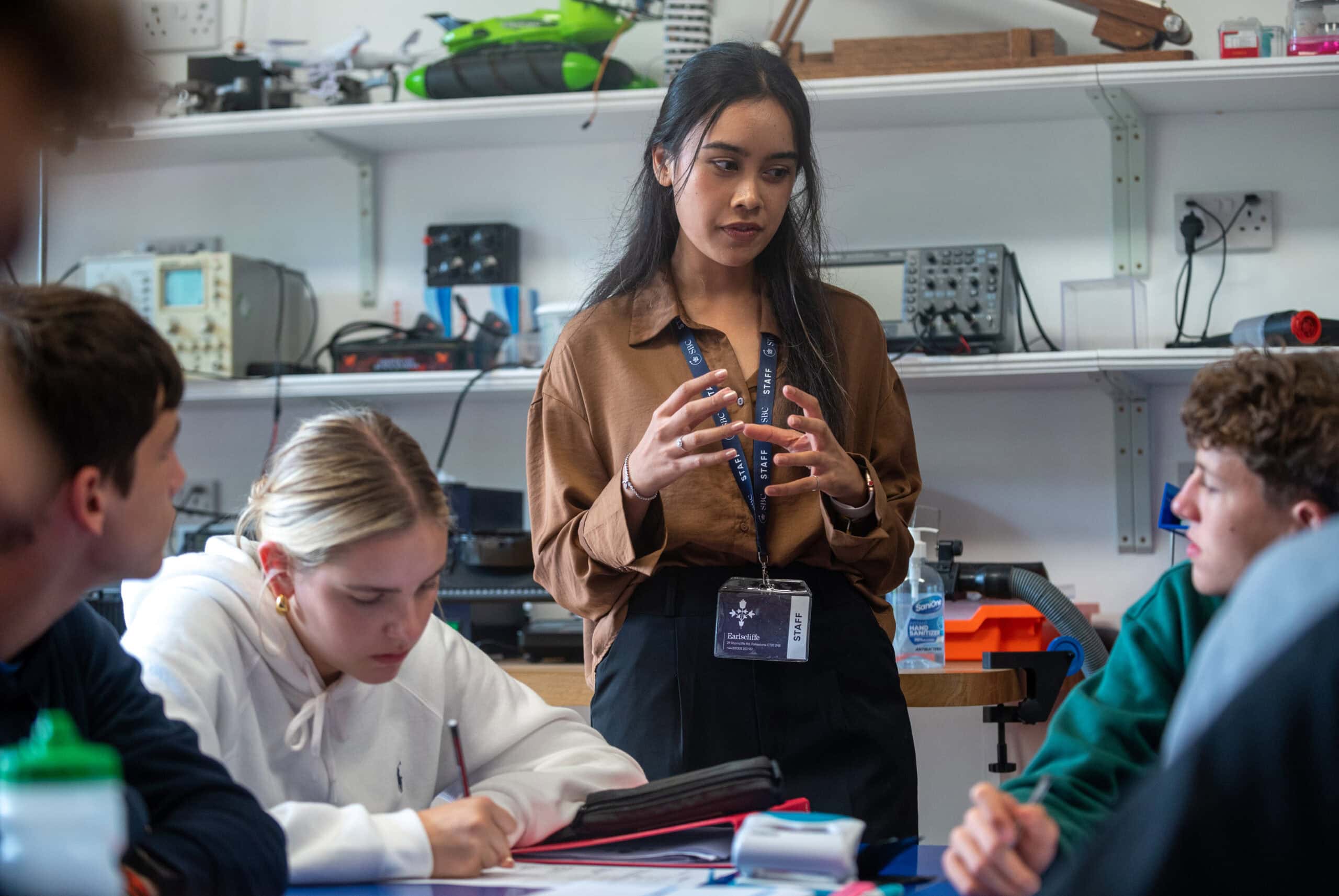 Advanced classroom with diverse students learning and taking notes, led by a young female teacher in a well-equipped lab at Summer Boarding Courses in the UK.