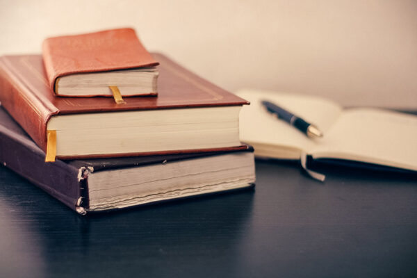 Books stack on a desk along with a notebook for writing