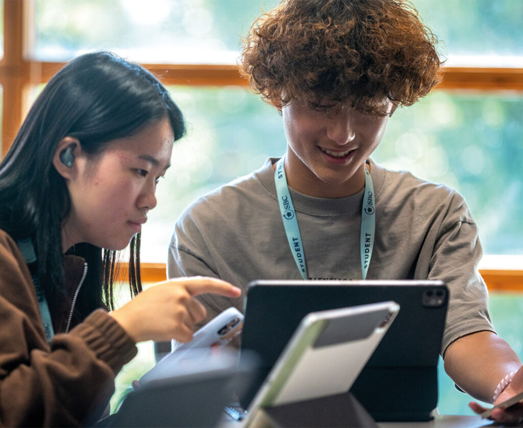 two-sbc-cambridge-business-students-using-tablet-and-phone-in-class