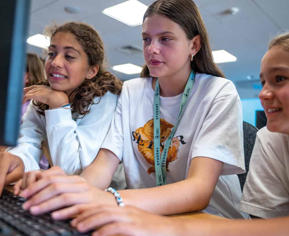Three female students working on the computer together, they are talking about work and typing together on the computer