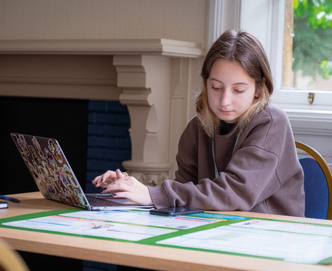 Female student looking down at her working while typing on her laptop in a Summer Boarding Courses classroom