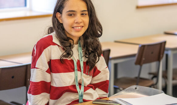 Female student sat at her desk in a Summer Boarding Courses class, she has he work and is smiling