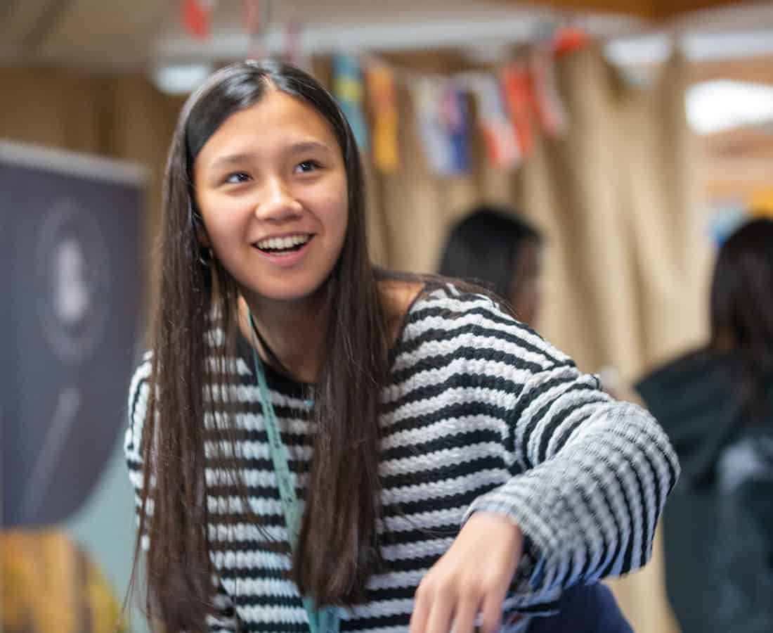 Female student smiling and playing ping pong with her friends at Cambridge College Summer Boarding Courses