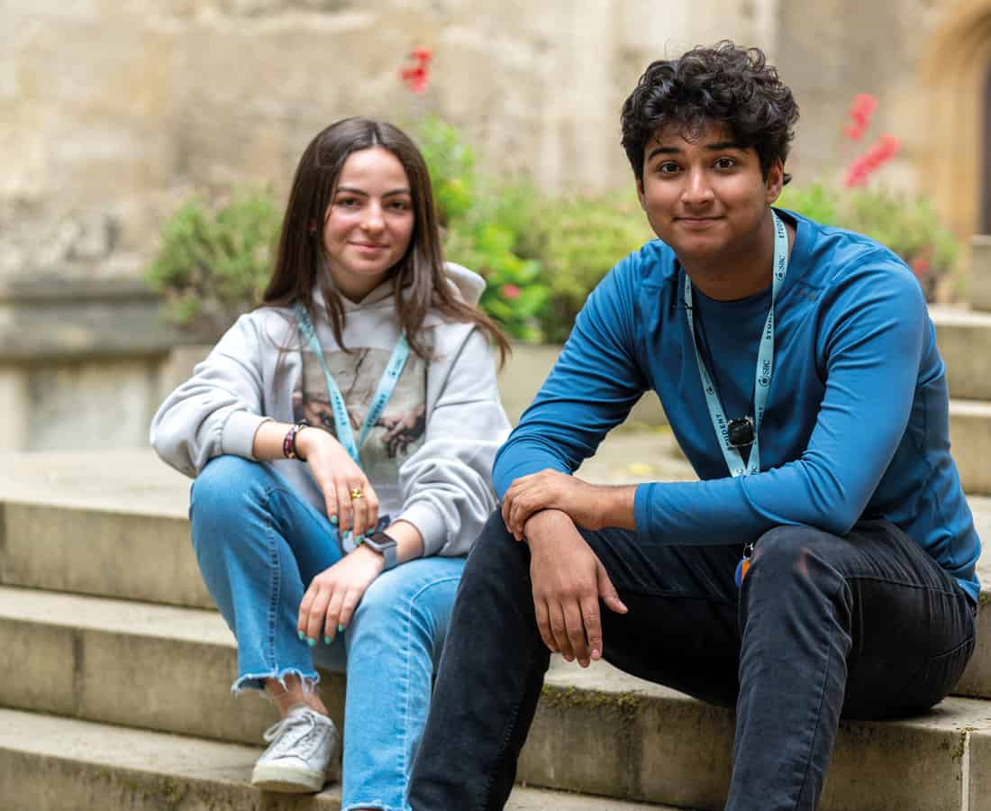 Male and female student smiling and sitting on the steps outside Oxford College at Summer Boarding Courses