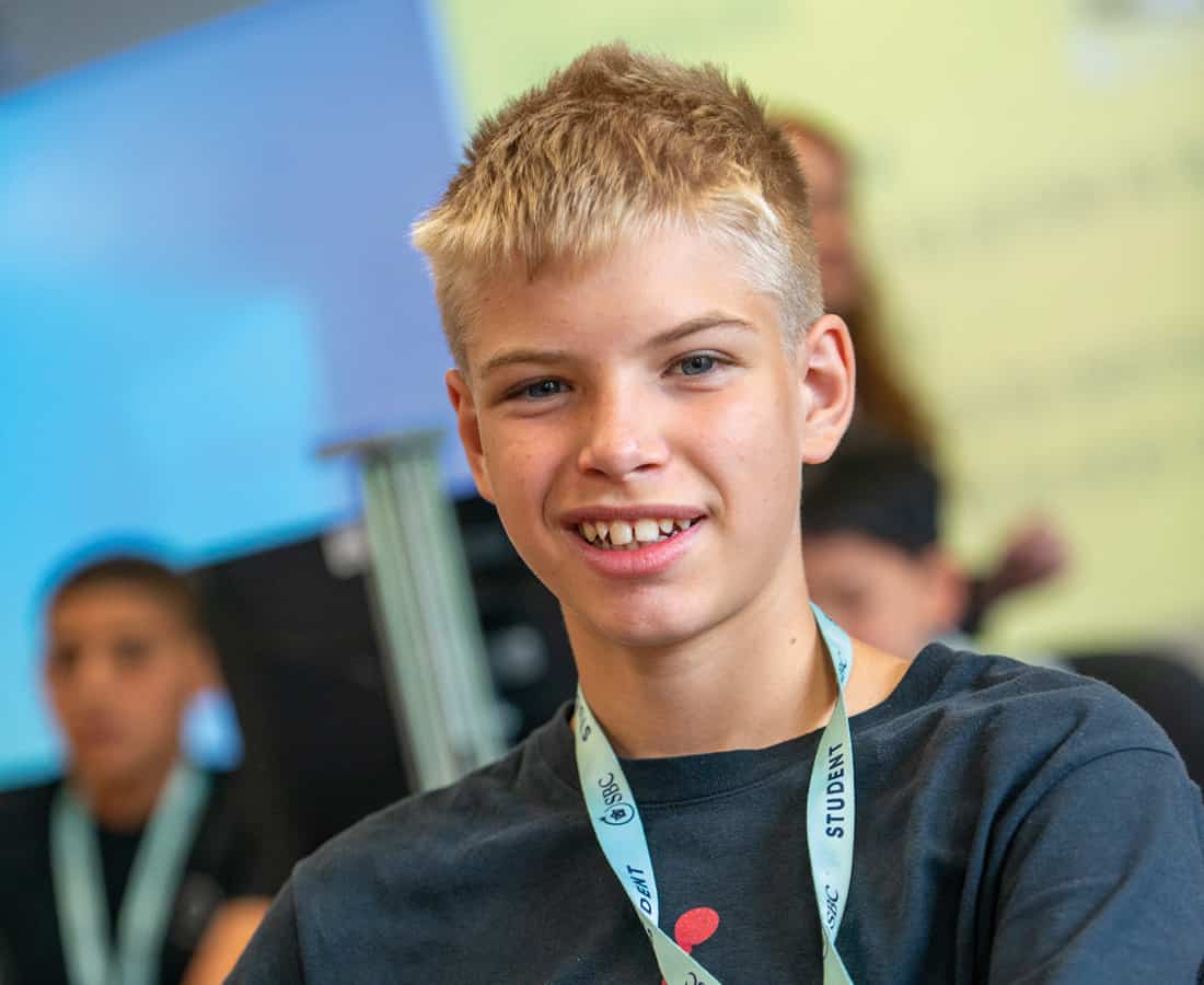 Male student smiling at the camera while usinga a computer in a Summer Boarding Courses classroom