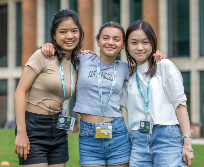 Three female Summer Boarding Courses students stood together smiling in the grounds of Headington Oxford