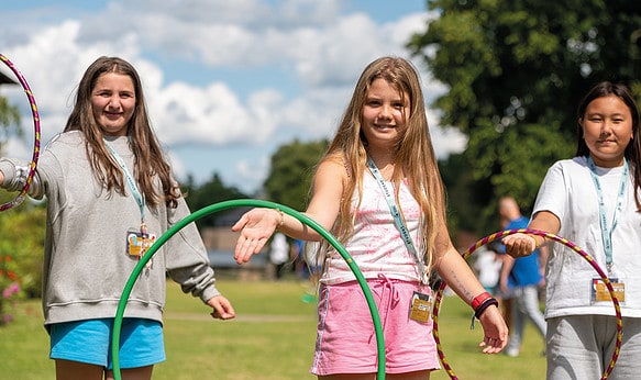 Three female students playing outside in the garden smiling and happy to be at SBC Canford summer school