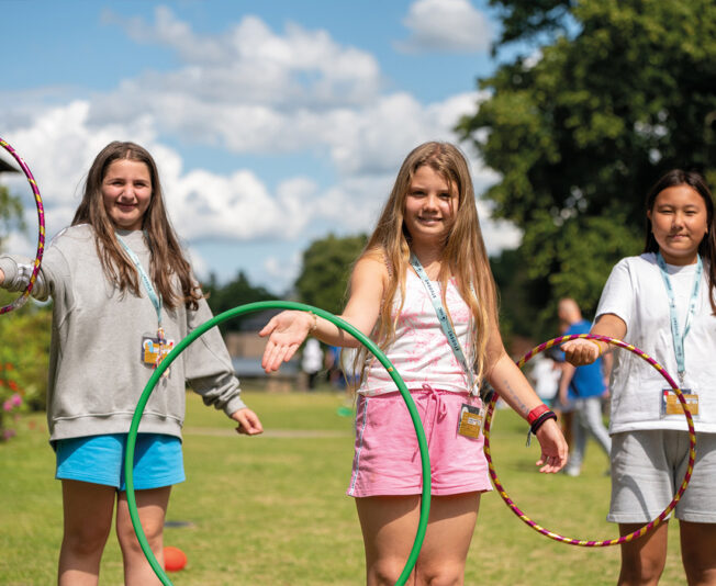 Three female students playing outside in the garden smiling and happy to be at SBC Canford summer school