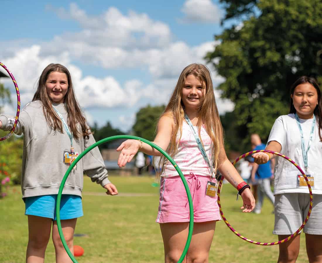 Three female students playing outside in the garden smiling and happy to be at SBC Canford summer school