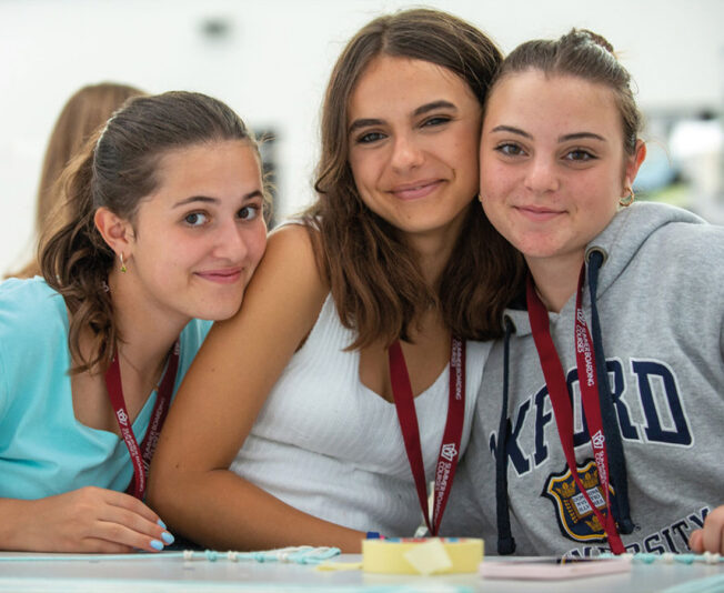 Three female students sat together in a Summer Boarding Courses class they are all smiling and having a good time