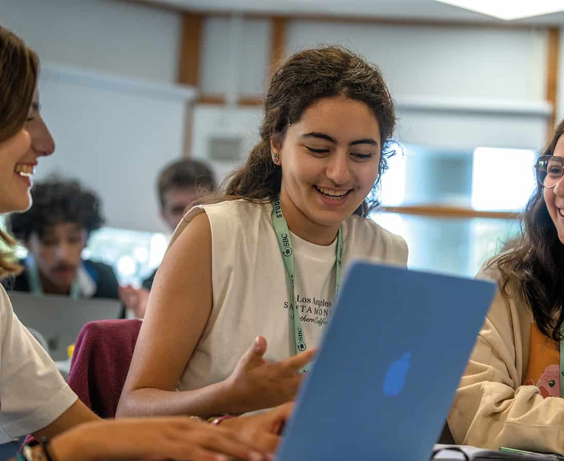 Three female students smiling and happy around a laptop discussing their time to shine presentation