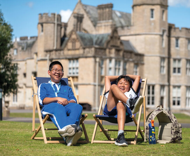 Two make students sat on deck chairs in the SBC Canford grounds both smiling and laughing at the camera