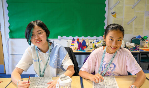 Two students in a classroom doing a social activity session, they are sat at a desk smiling while doing their activity sheets