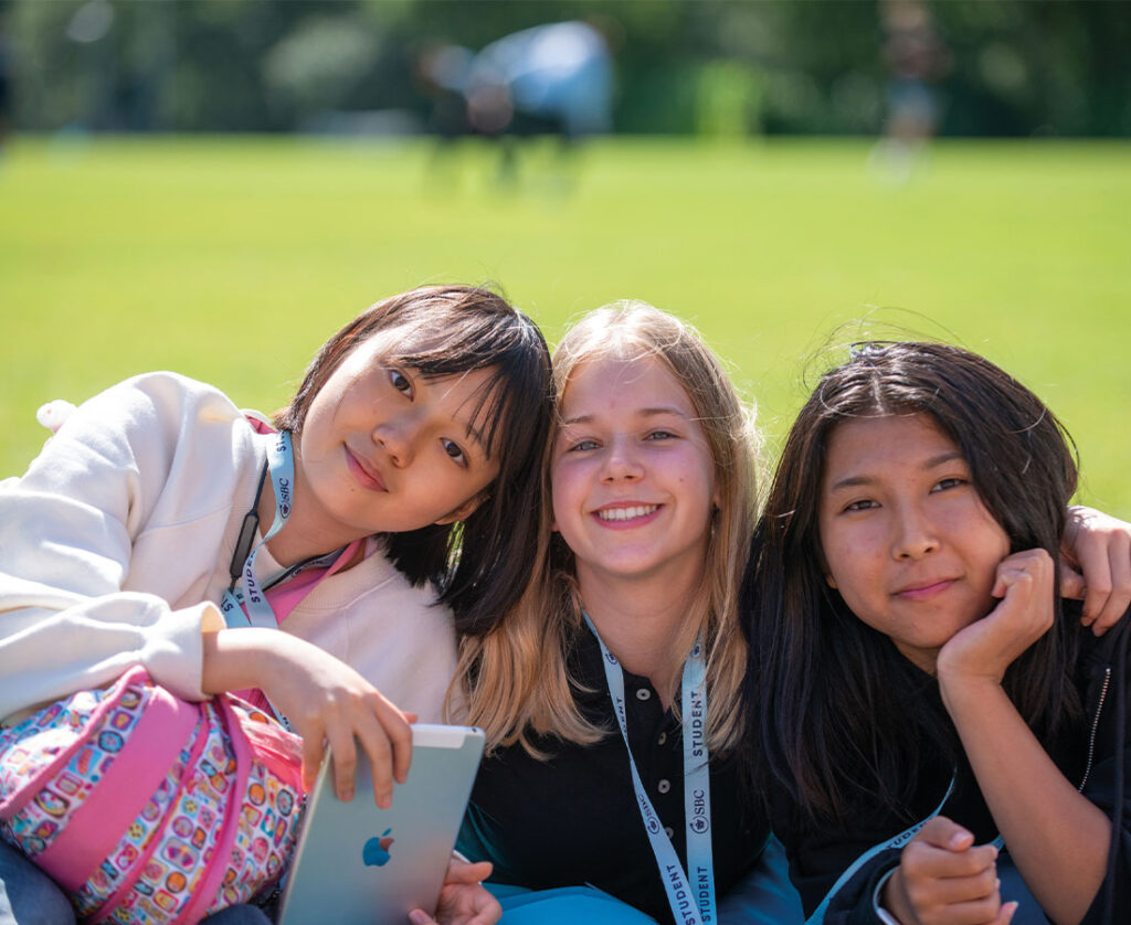 three-female-students-smiling-on-grass.