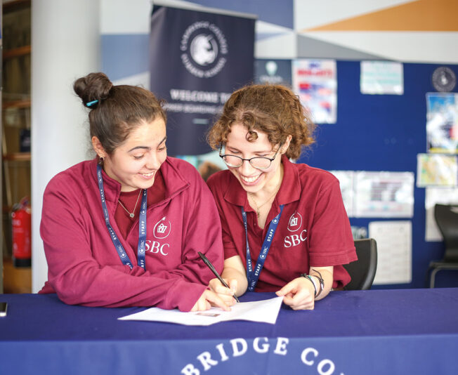 Staff at Cambridge College getting ready for students arrivals sat at the desk together with pens