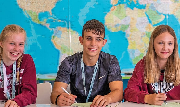 Three-smiling-happy-summer-school-uk-students-in-front-of-world-map-at-SBC-Headington