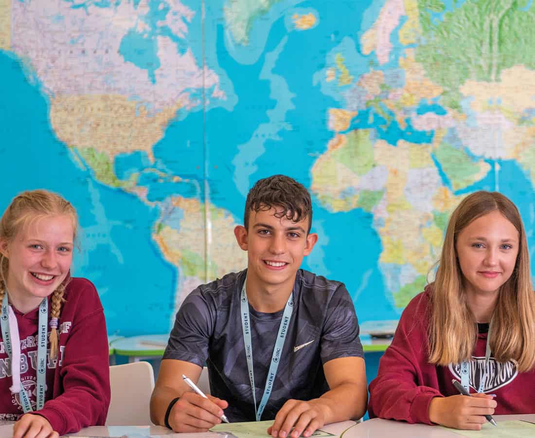 Three-smiling-happy-summer-school-uk-students-in-front-of-world-map-at-SBC-Headington