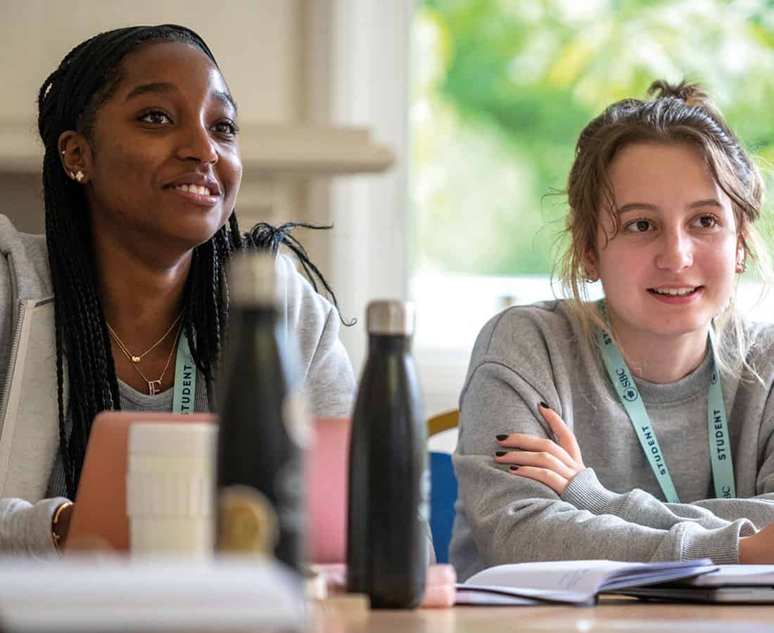 two-students-smiling-and-sitting-at-desks-with-waterbottles