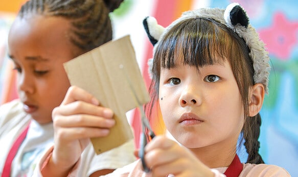 Female student cutting carboard for a craft activity at camp dragon