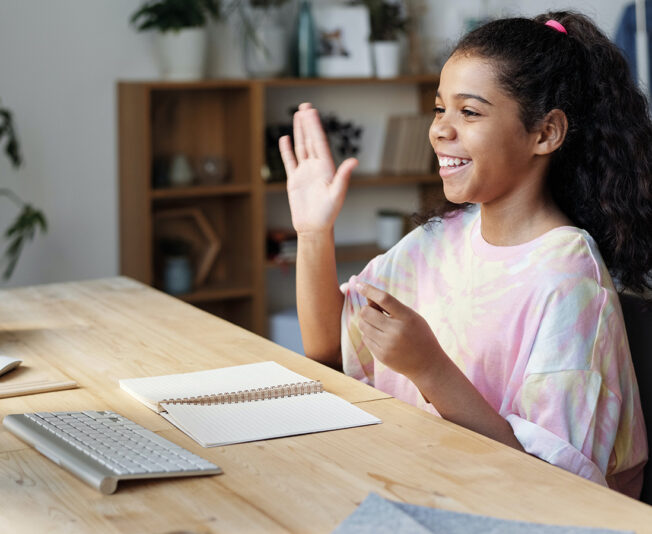 Girl-smiling-and-waving-at-the-computer-during-online-tuition-session