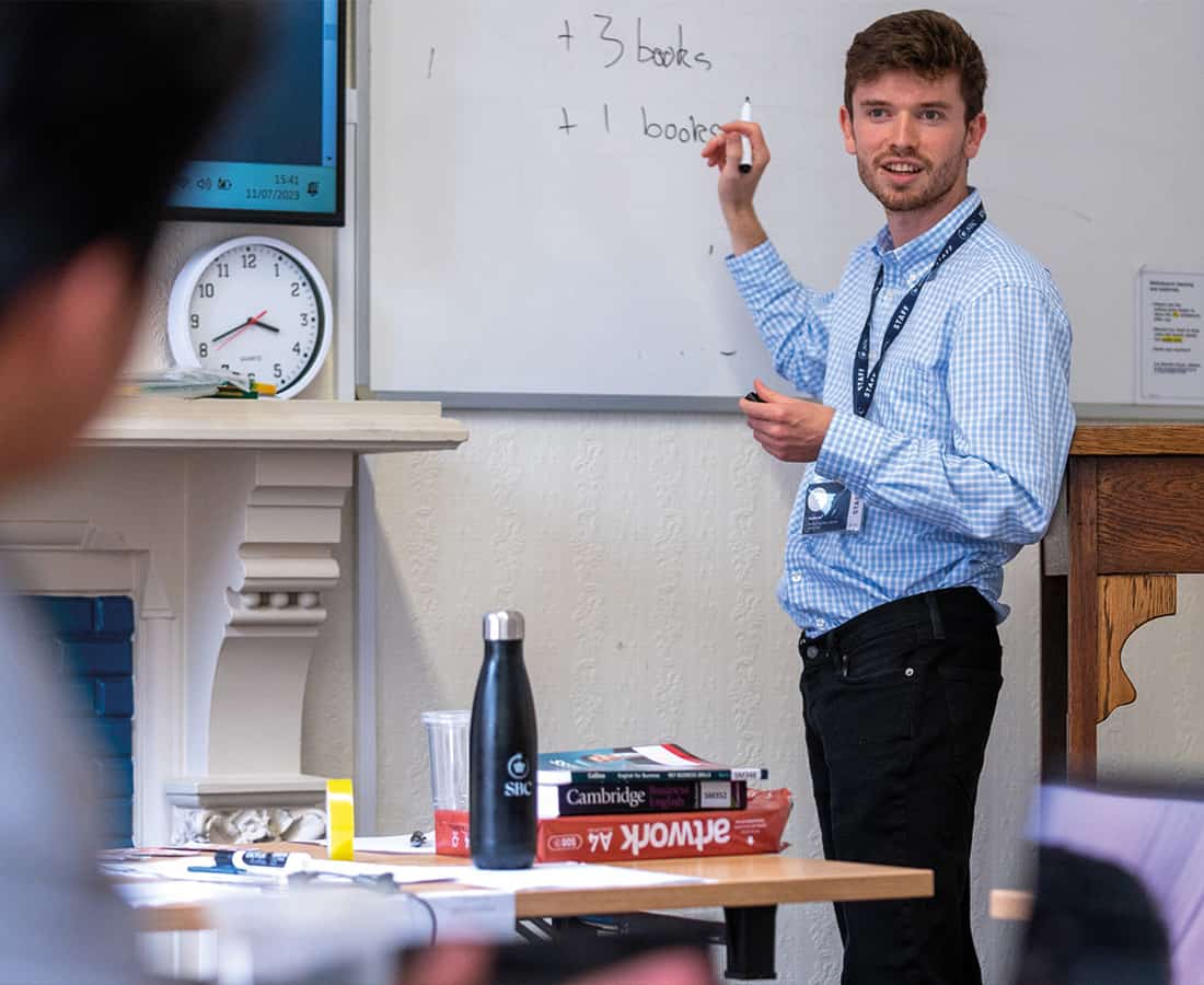 Subject tutor stood infront of a white board writing and teaching in a Summer Boarding Courses academic class
