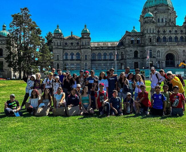A large group of students sits on grass in front of a domed government building