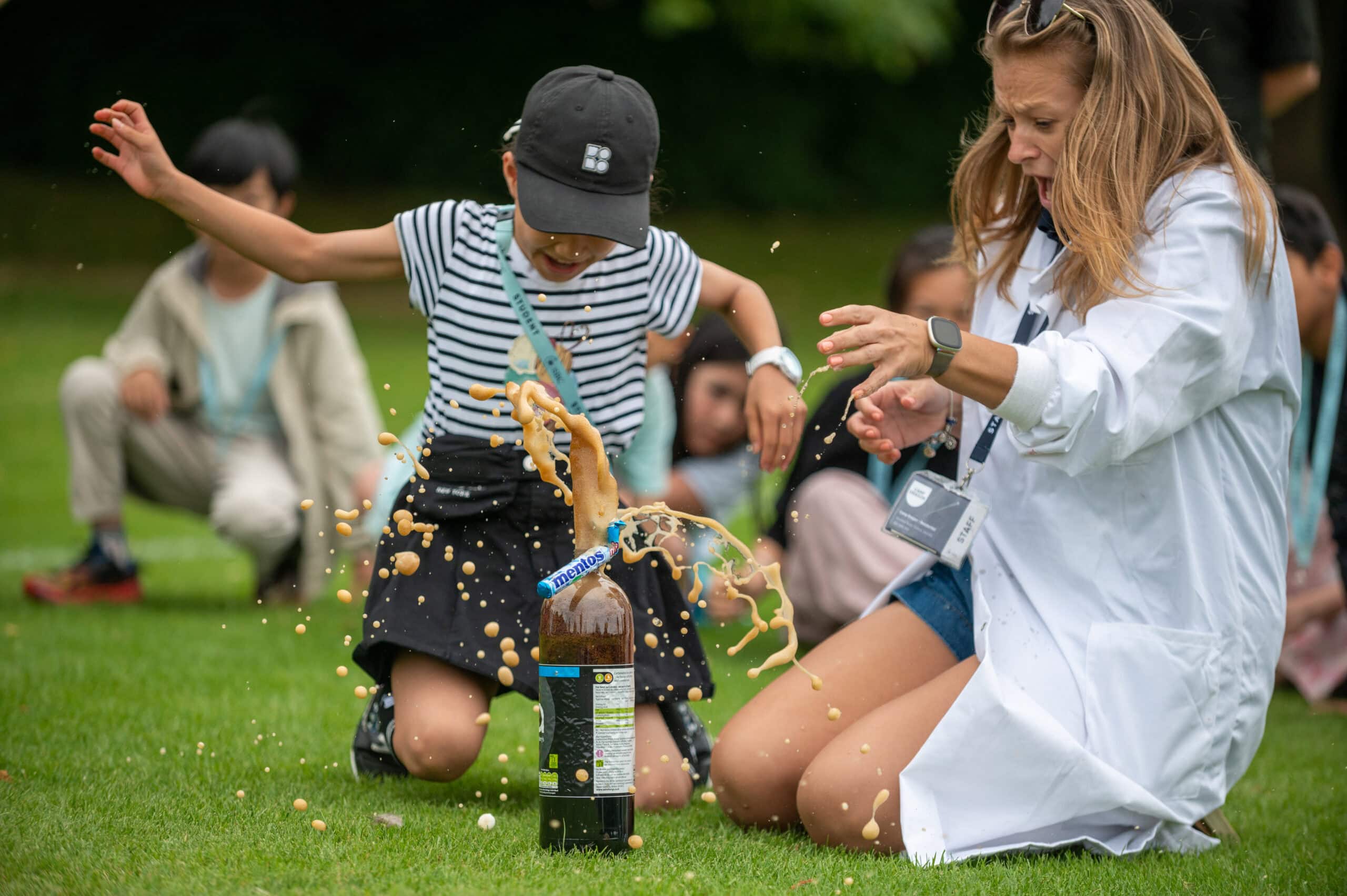 Bright young girl engaging in a fun science experiment with a teacher at a summer boarding course on a lush green field.