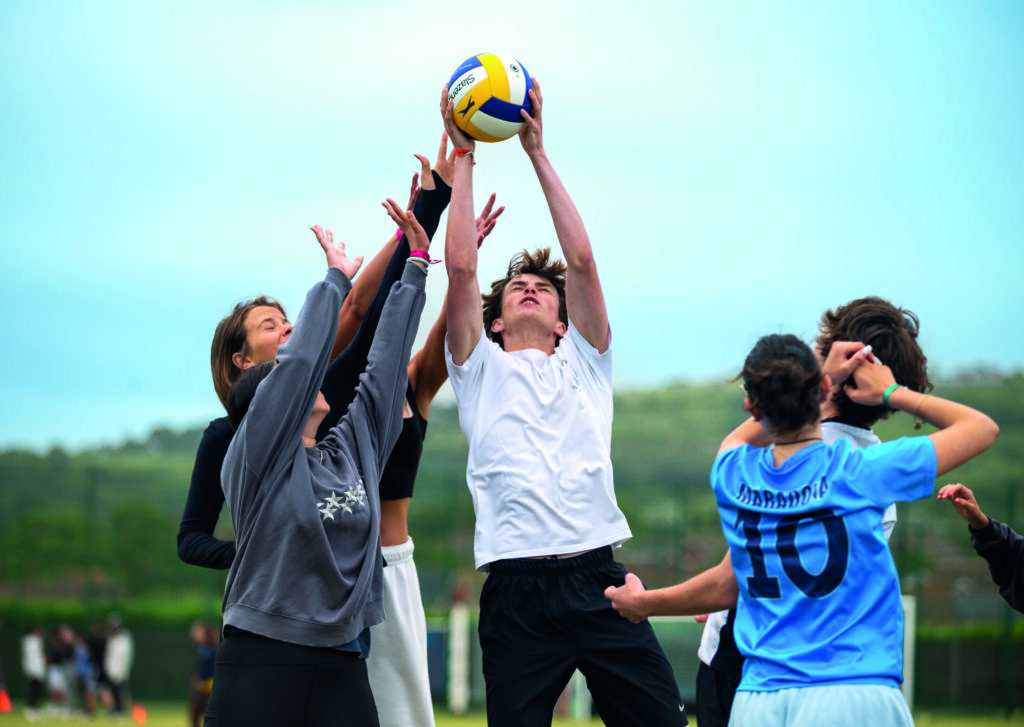 Youth playing volleyball at summer boarding camp on outdoor sports field