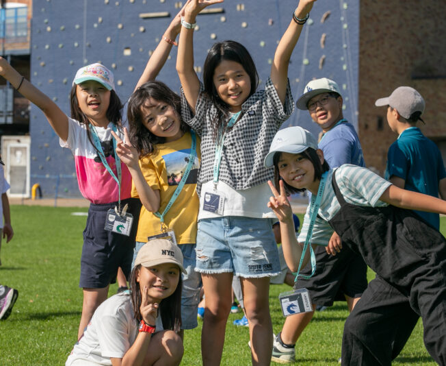 Vibrant group of children enjoying summer boarding courses outdoors with a climbing wall in the background.