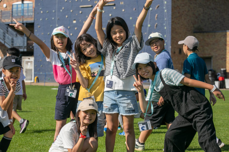 Vibrant group of children enjoying summer boarding courses outdoors with a climbing wall in the background.