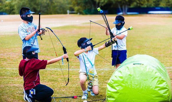 Archery activity at summer boarding courses for kids and teens on lush green outdoor field.