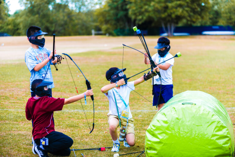 Archery activity at summer boarding courses for kids and teens on lush green outdoor field.