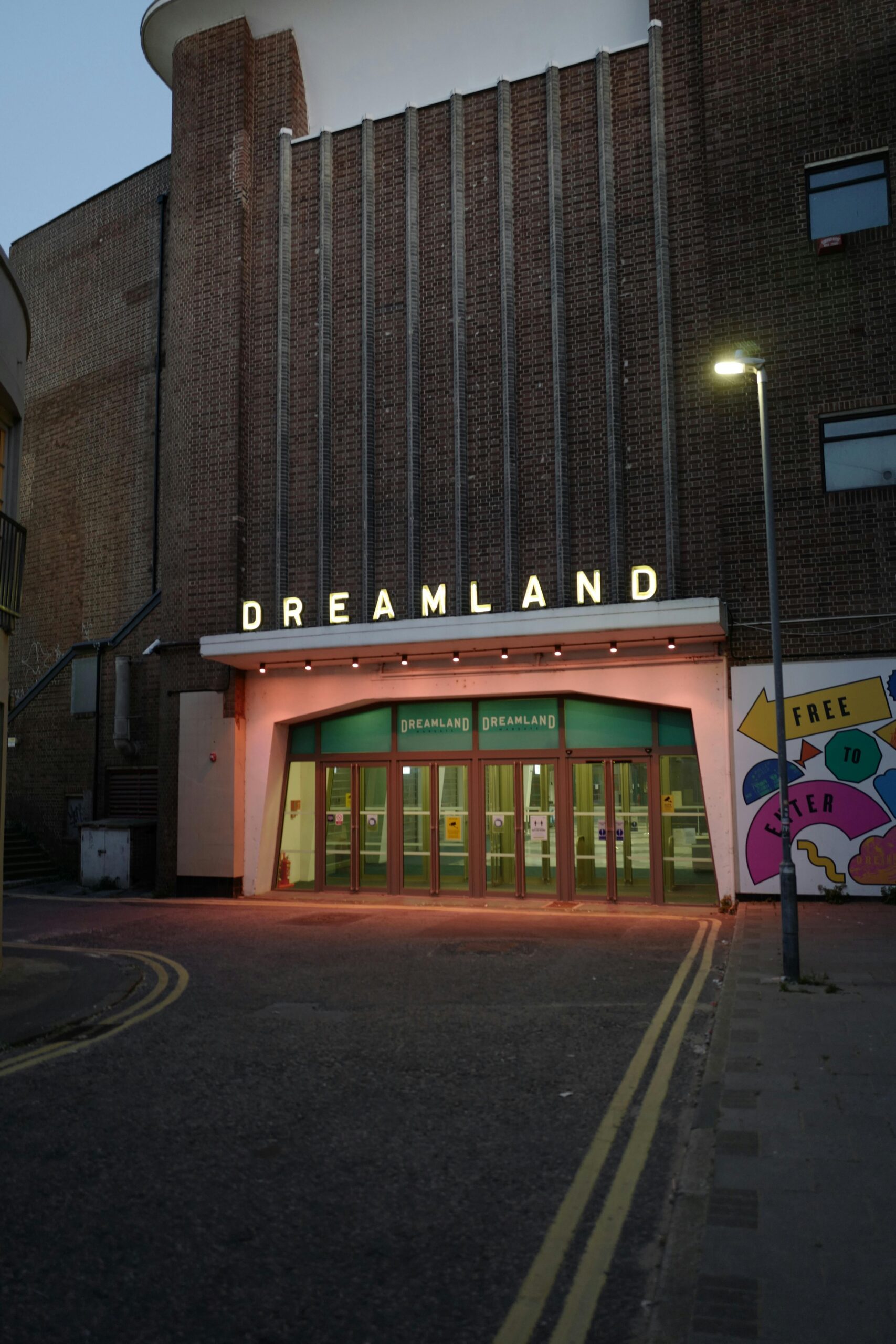 Dreamland amusement park entrance at night, brightly lit with retro signage and colourful exterior.