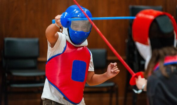 Bright blue fencing mask and red protective gear worn by children during fencing class at summer boarding course