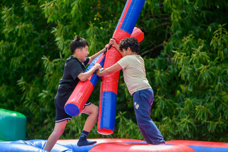 Two young students climb a red and blue inflatable pole game outdoors