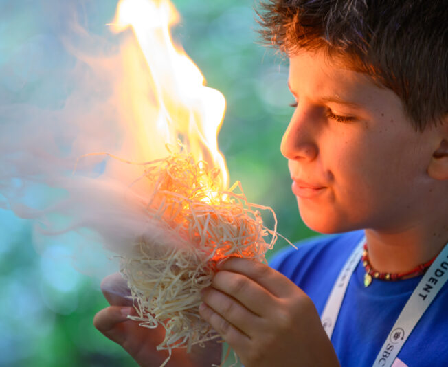 Young boy exploring science with a flame experiment during summer boarding courses, engaging in educational activities in a safe outdoor environment.
